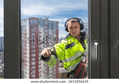 A Window Cleaner Operates at Height, Ensuring Views Are Clear and Buildings Shine in Urban Landscape Under Bright Sky