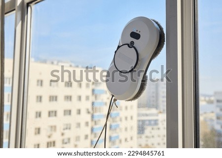 A window cleaner robot washes glass against the backdrop of multi-storey buildings