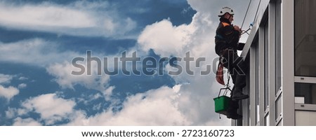 A window cleaner, secured with ropes, is working his way down the side of a modern building in an urban environment on a breezy day.