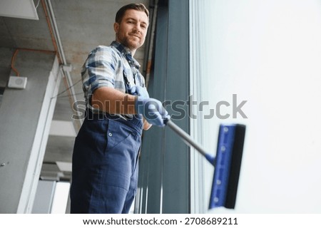 Window cleaner using a squeegee, diligently washing windows in a sleek, modern office building with a stunning glass facade