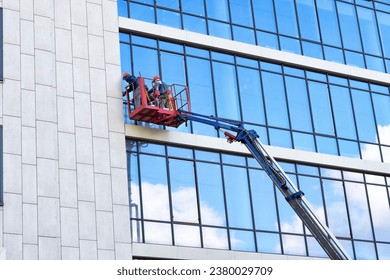 Window cleaners clean the glass windows of a building at height on a lifting platform. A worker polishes glass, washes windows of an office building in a crane bucket.
