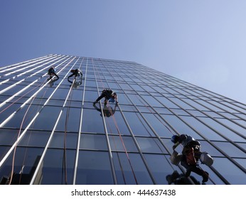 Window cleaners washing office windows with ropes