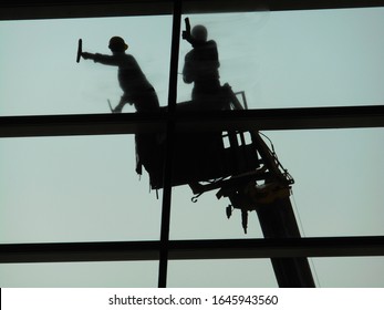 Window Cleaning High Building By Two Workers Standing In Crane Cradle A Silhouette Shoot Taken From Inside Building