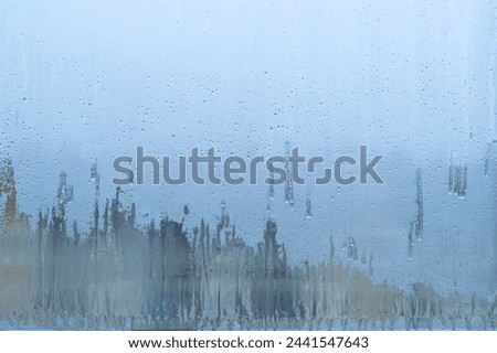 A window with condensation on it. The condensation are in the form of droplets and are scattered across the window. The window is foggy and the view outside is blurry