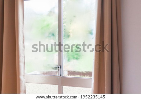 Window with condensation of steam after heavy rain. Bright morning sun in the window through the curtains. Texture or background photo with copy space