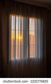 Window with curtains that allow a glimpse of the sunset