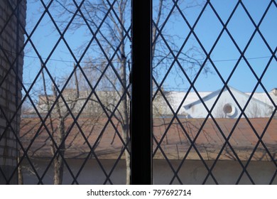 A window with a diamond-shaped lattice. Roofs and buildings outside the window.