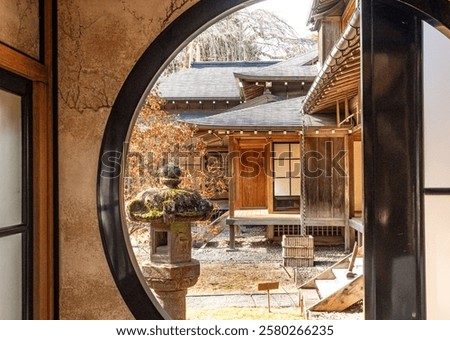 Window frame, a beautiful round window view from the inside of a traditional Japanese house into a Japanese garden at daytime in winter at the Tamozawa Imperial Villa Memorial Park in Nikko, Japan.