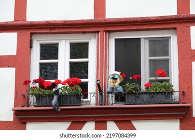 window of a german half timbered house decorated with red flowers and funny statues