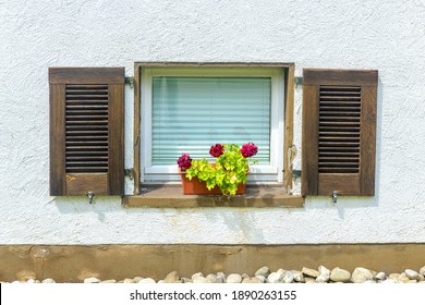 Window Of Home Basement With Nice Flowers And Wood Shutters, White Plastered Outside Wall And Stones Of Landscape Design. Front View Of Beautiful Residential House Exterior In Summer.