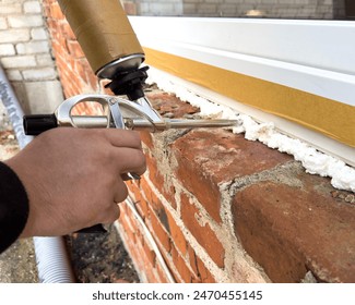 Window installation. The process of insulating windows with construction foam. A builder's hand seals the cracks between the building and the window frame. Construction and insulation of the building.
