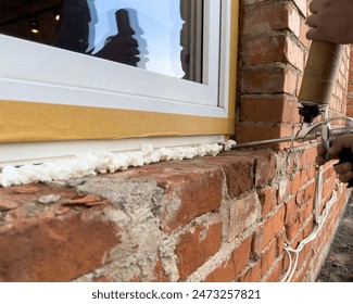 Window installation. The process of insulating windows with construction foam. A builder's hand seals the cracks between the building and the window frame. Construction and insulation of the building.