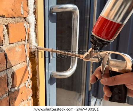 Window installation. The process of insulating windows with construction foam. A builder's hand seals the cracks between the building and the window frame. Construction and insulation of the building.