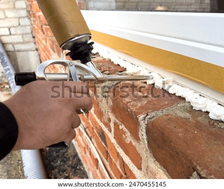 Window installation. The process of insulating windows with construction foam. A builder's hand seals the cracks between the building and the window frame. Construction and insulation of the building.