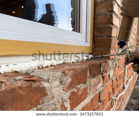 Window installation. The process of insulating windows with construction foam. A builder's hand seals the cracks between the building and the window frame. Construction and insulation of the building.