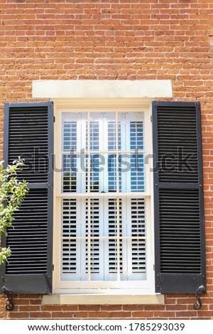 A window in an old federalist building has black shutters on the outside and white shutters on the inside.