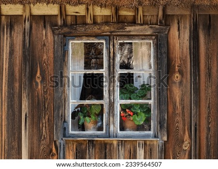 The window of an old, historic wooden cottage, with flowers and curtains