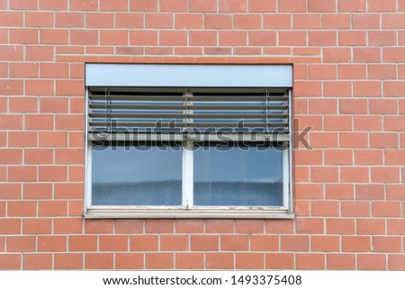 A window on a brick wall with half-lowered shutters.