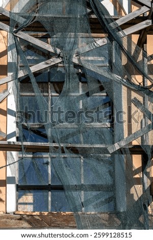 A window on the facade of an old building covered with scaffolding and netting.