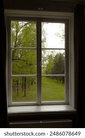 A window with an open pane opens up a view of the river with a forest and a path on the sides. The landscape of the park with the river on the horizon through the window.