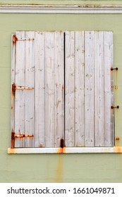 Window protected by closed white wooden shutters on a light green wall.