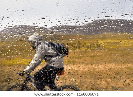 Window in rain drops and man on mountain bike rides on the country road out of focus.