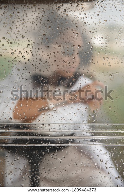 Window\
with rain drops and woman figure with dark hairs in white suite\
with sunglases and with watches on the golf\
car