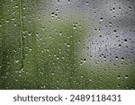 Window with raindrops on it. The raindrops are small and scattered, creating a blurry effect. Scene is calm and peaceful, as the raindrops fall gently on the window