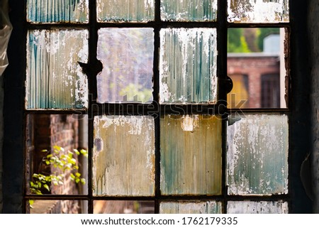 Window of a ruined factory with old brocken glass and rusty iron in a brick wall in a lost place in Germany. Colorful background with transparent elements of industrial heritage building in Iserlohn.
