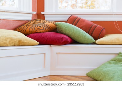 Window seat with colorful pillows. Close up bright sunny image. Warm, casual, inviting, fun interior space. Horizontal