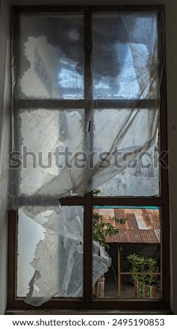 a window that has a four-box design covered with transparent plastic that looks worn and torn