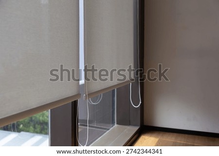 A window with two white curtains, one of which is pulled back. The curtains are tied to a cord, and the room has a wooden floor. white blind rolling curtain in the office.
