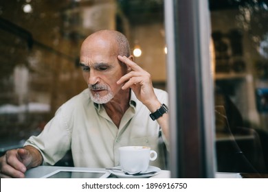 Window View Of Aged Caucasian Male User Connecting To Public Internet In Coffee Shop For Browsing Web Information Via Digital Tablet Gadget, Senior Man Reading Online Article Feeling Puzzled Indoors