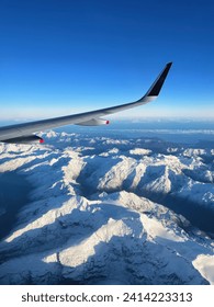 Window view from a flight looking over new zealand south island scenery. Snow mountain from aircraft flying into queenstown nz. Winter flying over glacier landscape.