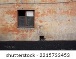 A window in wall of an old Soviet building in the Kazakh city of Pavlodar. Peeling orange paint on concrete wall. Wooden frame in window opening. The concept of dilapidation, old age and devastation