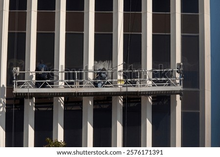Window washers on scaffold on large commercial buildng with linear columns. There is soap on the window
