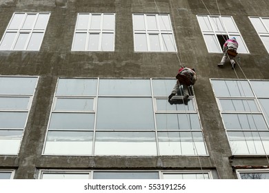 Window washers on top. Two workers hung ropes wash windows on high-rise.