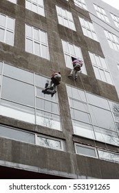 Window washers on top. Two workers hung ropes wash windows on high-rise.