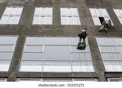 Window washers on top. Two workers hung ropes wash windows on high-rise.