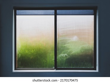 Window With Water Droplets Of Humidity Condensation On Window Seen From Indoor With Backyard Bokeh Behind It