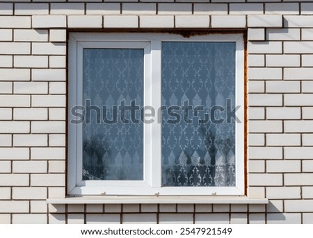 A window with a white curtain and a brick wall behind it. The curtain is drawn, and the reflection of the curtain can be seen in the window