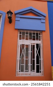 A window with a white frame and bars on it. The window is on a building with a blue and orange color scheme