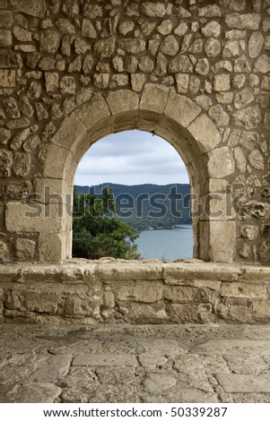 A window/arch at the entrance of a romanesque church in a spanish village. A beautiful landscape may be seen through it.