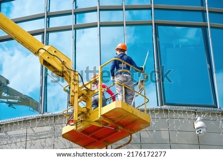 Windows cleaning work, female workers team washing glasses windows at height in lifting platform. Window washing on office building in crane bucket. Window cleaners, building exterior wet wash