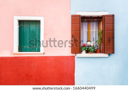 Windows on the red and blue painted facade of the house. Colorful architecture in Burano island, Venice, Italy.