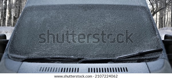 Windscreen wipers and a snow covered car\
or bus.winter season. front view. A frozen car windshield is\
covered in ice and snow on a winter day. Close-up\
view.
