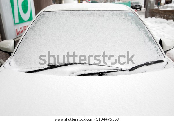 Windscreen wipers and a snow\
covered car.Front view of car is fully covered with snow after\
snowstorm