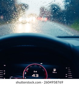 Windshield full of raindrops while driving on a road rainy weather at dusk driver's point of view