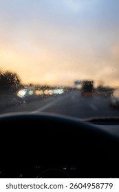 Windshield full of raindrops while driving on a road rainy weather at dusk driver's point of view