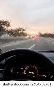 Windshield full of raindrops while driving on a road rainy weather at dusk driver's point of view